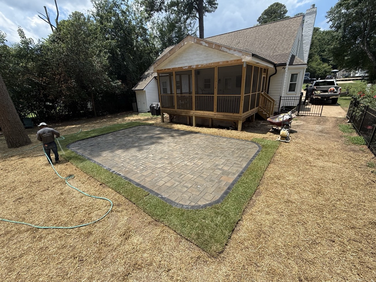 A freshly laid paver patio behind a screened porch, edged and border-set, with new sod knitting in around it.